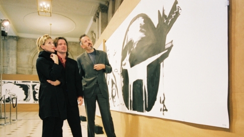A photo of three people, one woman and two men, standing in front of one of the original drawings by Bono of "Peter and the Wolf".