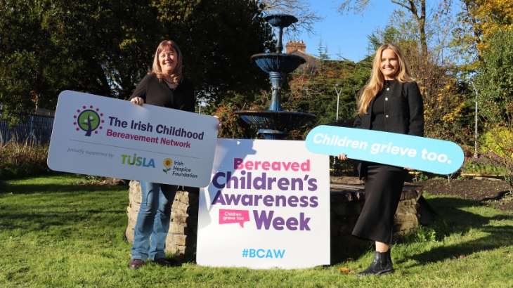 A photo of two women standing outside, holding signs for Bereaved Children's Awareness Week 2023.