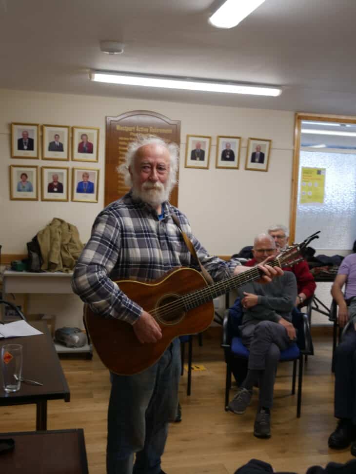 A photo of a man named Tony Reidy playing a guitar at a Men's Shed gathering in Westport.