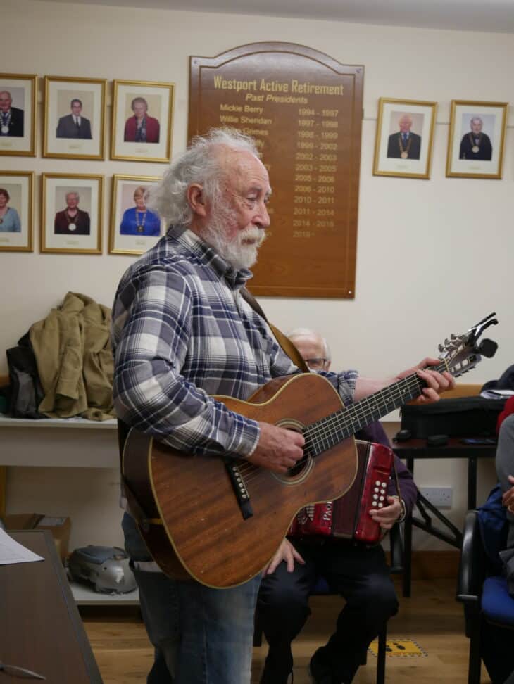 A photo of a man named Tony Reidy playing a guitar at a Men's Shed gathering in Westport.