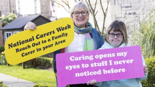 A photo of two women holding up signs to promote Carers Week 2024. Irish Hospice Foundation is one of the charity partners taking part in Carers Week from June 10 - 16, 2024, organised by Care Alliance Ireland.